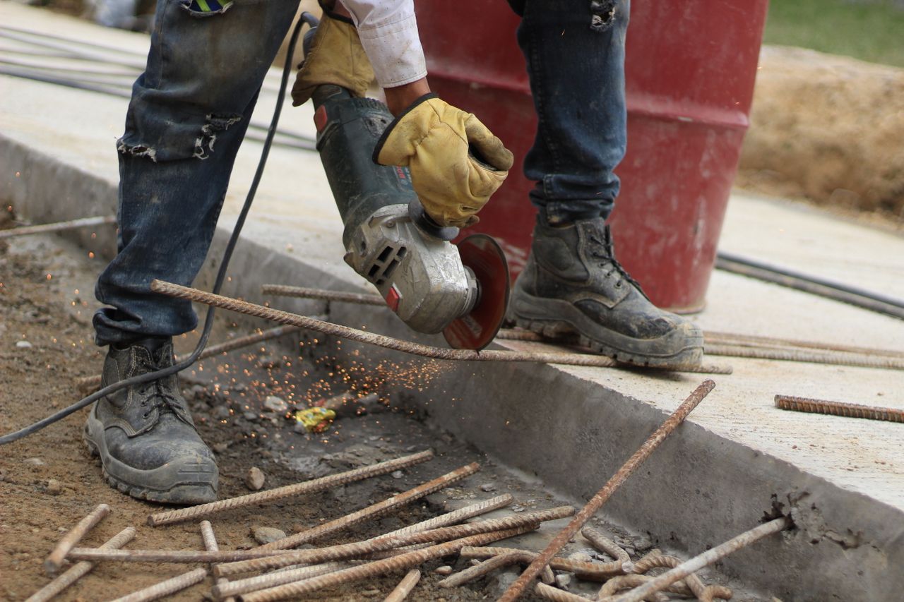 Close-up of a worker using an angle grinder to cut steel bars on a construction site.